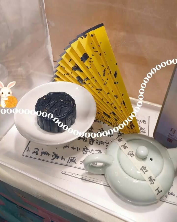 Patterned baked mooncake on a plate with a ceramic teapot and paper fans